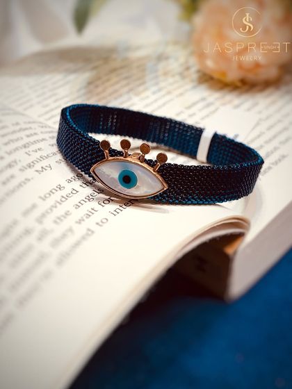 A modern take on the Evil Eye, this bracelet features the symbol in mother-of-pearl, set in a crown-like gold frame on a dark blue mesh band. It’s a chic and powerful accessory.