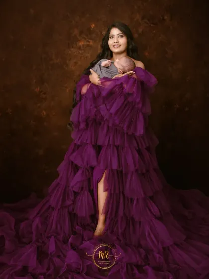 A smiling mother holds her newborn baby, wrapped in a simple grey cloth that contrasts beautifully with her vibrant purple dress.