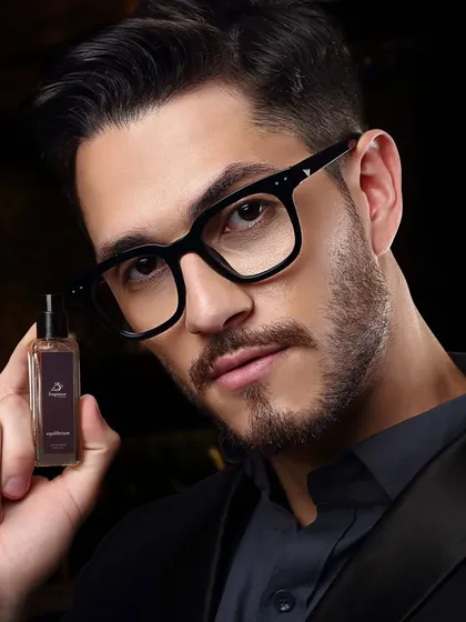 A close-up of a model presenting a perfume bottle. The intense gaze and dark background create a mysterious and alluring mood for the product.
