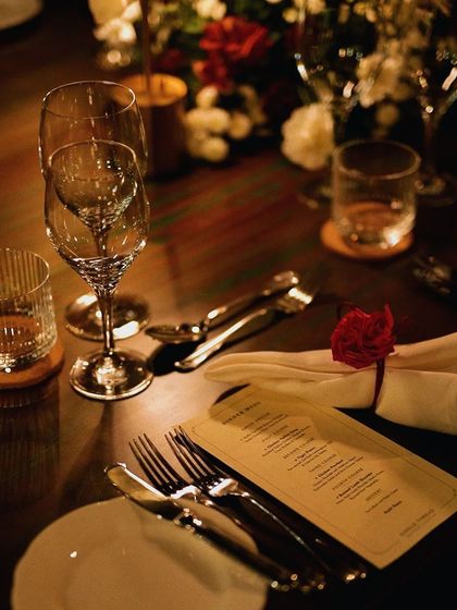 A beautifully set table in a dimly lit, intimate setting. The personalized menu and single red rose add a touch of romance and sophistication.