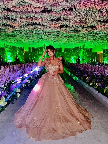 A client looking like a princess in a champagne-colored ball gown, set against a stunning floral backdrop. This is the epitome of reception glamour.
