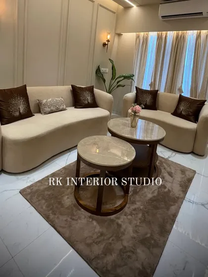 A full view of the living room, showing how the curved sofas, nested center tables, and plush rug come together to create a cohesive and inviting space. The wall mouldings and ambient lighting complete the luxurious feel.