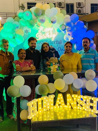 A family posing in front of the pastel birthday decor at night, showing how the neon and light-up signs create a festive glow.