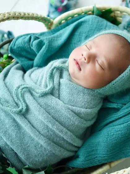 A close-up on the baby's face, framed by the teal bonnet and wrap, highlighting their peaceful expression.