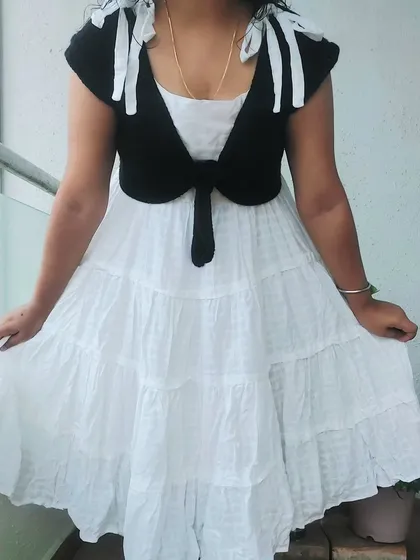 This is the Mari Top, a versatile tie-front shrug that can be layered over dresses or tops. The white bows on the shoulders add a playful touch.