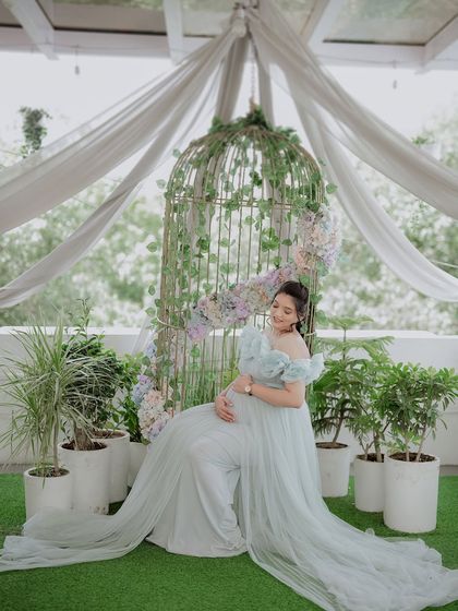 Seated gracefully, this mom-to-be shows how comfortable and beautiful our rental gowns are. The garden-themed studio setup with the birdcage adds a whimsical touch to the maternity photo.