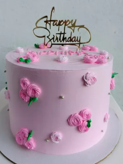 A tall pink cake decorated with small, delicate piped roses and silver pearls.