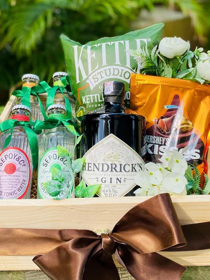 A sophisticated gift for the gin enthusiast, this hamper is built around a bottle of Hendrick's Gin. It is complemented by artisanal tonic water, kettle-cooked chips, and Hershey's Kisses, presented in a simple yet elegant wooden tray with a rich brown ribbon.