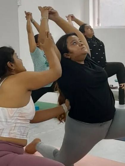An instructor offers a gentle assist in Anjaneyasana (Low Lunge), helping a student find a deeper and safer stretch.