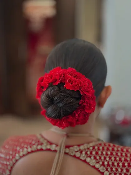 A clean and classic bridal juda, beautifully encircled with a vibrant red floral gajra. This is a signature look for the main wedding day, designed to perfectly complement a traditional red lehenga.