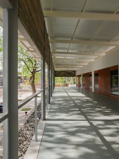 Dappled light filters through the trees and onto the covered veranda of a multi-use pavilion in Ahmedabad. This transitional space blurs the boundary between inside and outside, offering a shaded retreat that is connected to the surrounding landscape.