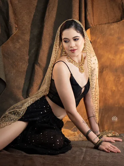 A relaxed, seated pose in a modern fusion outfit. The combination of a contemporary top with a traditional draped skirt and dupatta creates a unique and stylish look.