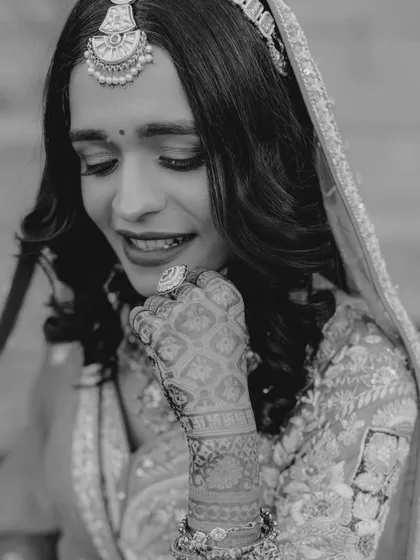 A candid black and white shot of the bride smiling. This captures a moment of genuine happiness and shyness, showing her beautiful henna-adorned hand.