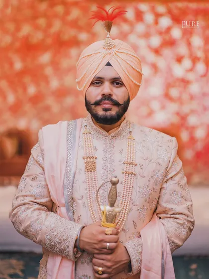A powerful portrait of the groom holding his kirpan. The soft, warm background contrasts beautifully with his confident and regal presence.