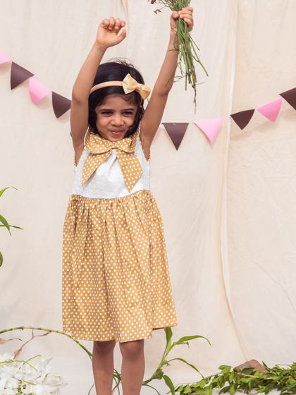 Celebrating in a cute mustard yellow polka dot dress. The oversized bow at the collar adds a touch of whimsy to this cheerful and playful outfit.