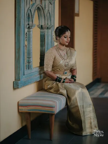 A full view of the bride seated, showcasing the elegant drape of her gold silk saree and the detailed craftsmanship of her custom blouse.