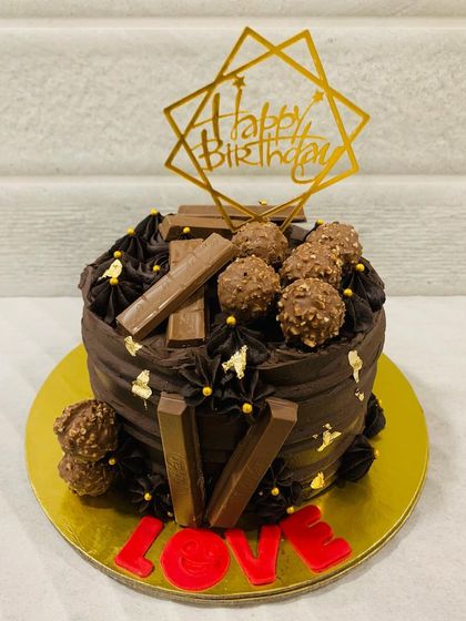 A rich chocolate truffle cake decorated with KitKat bars, Ferrero Rocher, and the word "LOVE" in red fondant. A perfect gift for your favorite person.