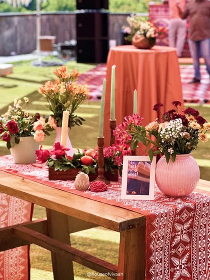 A close-up of a rustic wooden bench with a traditional patterned runner and arrangements of colorful flowers, capturing the earthy and vibrant essence of the Pahadi theme.
