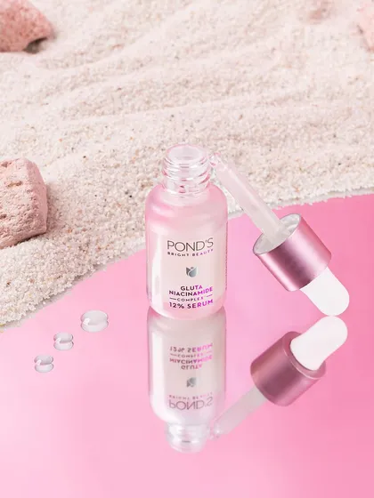 This visual for Pond's Bright Beauty serum uses a reflective surface and sand to create a sophisticated, beach-inspired scene. The reflection adds depth and elegance to the product shot.