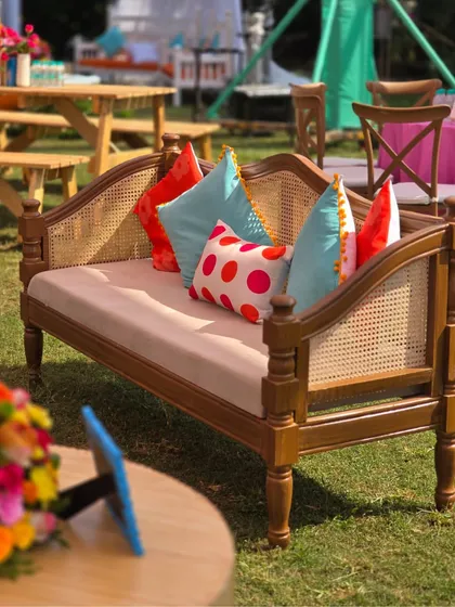A comfortable and stylish seating area for guests, using a rattan-backed sofa and bright, patterned cushions that match the event's artistic and colorful theme.