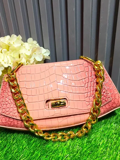 This pink bag with a crocodile skin texture and a chunky gold chain strap is a trendy, high-fashion accessory to complete your look.