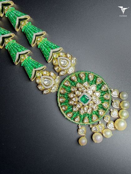 A detailed view of a modern-traditional necklace, showcasing a central emerald surrounded by polki diamonds and south sea pearls.