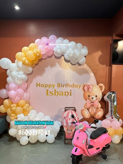 A sweet teddy bear theme for Ishani's first birthday. The decor includes a pastel balloon arch on a round backdrop, a cute teddy bear cutout, and a pink toy scooter as a prop.