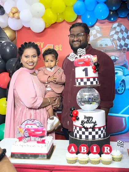 A lovely family portrait with their son on his first birthday, posing proudly with their Cars-themed cake.