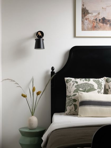 Even the smallest spaces can feel meaningful. This compact bedroom features a classic black bed, a simple green side table, and a modern wall sconce, proving that functional design can also be beautiful.