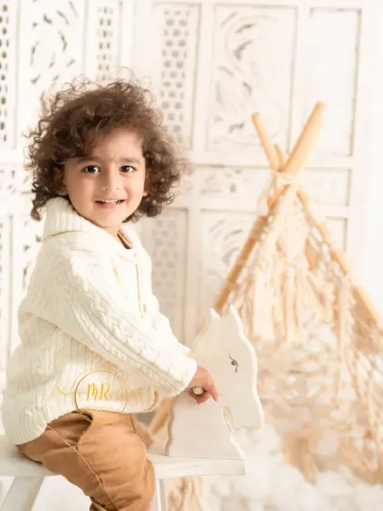 A toddler boy enjoys a ride on a wooden rocking horse in a simple and classic studio setup.