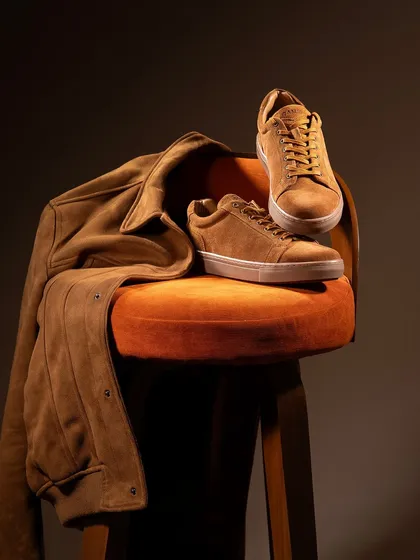 A classic still life of brown suede sneakers and a matching jacket. The monochromatic color scheme and warm lighting create a sophisticated and cohesive look.