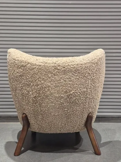 The back view of our unique bouclé accent chair, showing its curved form and sturdy, angled wood legs.