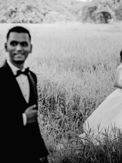 A black and white portrait in a field, with the groom in the foreground and the bride in the background. This composition creates depth and a sense of story.