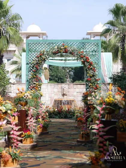 The entrance to the 'Tales of Tropica' event featured a beautiful floral arch of warm-toned flowers, set against a lattice screen and surrounded by lush tropical plants.