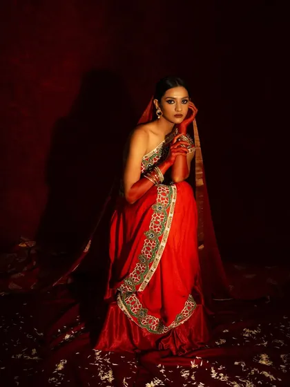 A full-length portrait from a bridal editorial, using a rich, monochromatic red palette. The model, in a beautifully embroidered saree, is seated in a way that feels both regal and contemplative.