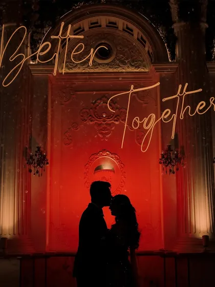 A powerful silhouette shot against a grand, illuminated backdrop. This image captures the romance and drama of a cocktail night, symbolizing the couple's unity with the phrase "Better Together."