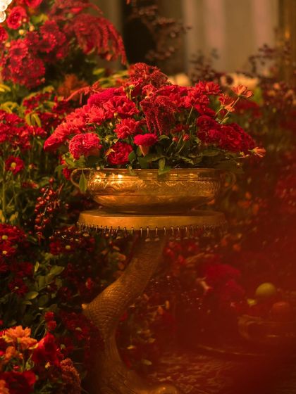 A detail shot of a floral arrangement in a beautiful brass urn. The combination of different shades of red flowers and the metallic accent creates a look of pure luxury.