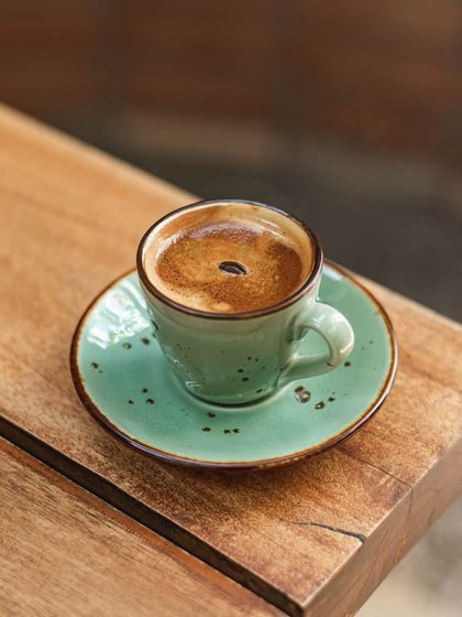 A classic espresso shot served in our rustic green ceramic cup, with a single coffee bean for garnish.