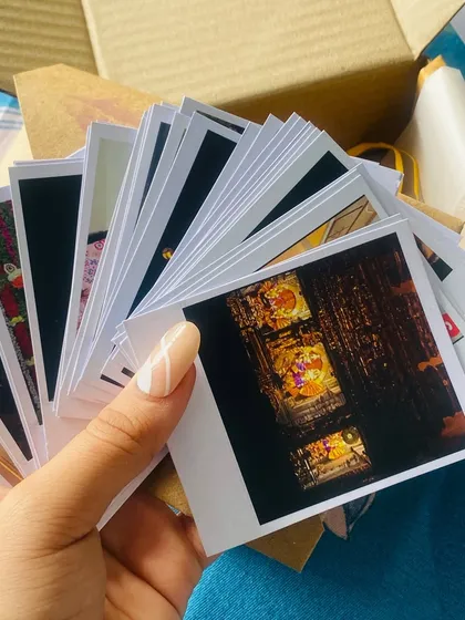 A hand holding a fanned-out stack of freshly printed Polaroids, showing the crisp black borders and vibrant images within.