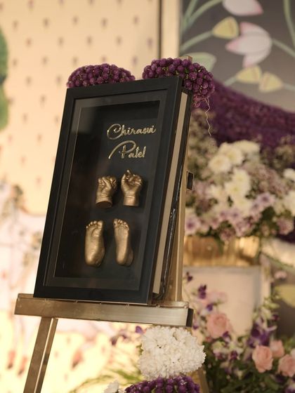 A close-up of a personalized decor element for a naming ceremony. This framed casting of the baby's hands and feet is a beautiful keepsake and a touching part of the event's decoration.