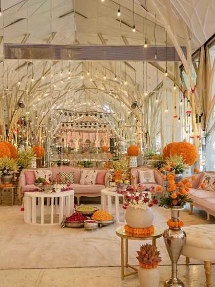 A beautiful indoor Mehendi setup combining soft pastel lounges with vibrant pops of marigold. The modern, airy venue is transformed into a festive space perfect for a morning celebration.