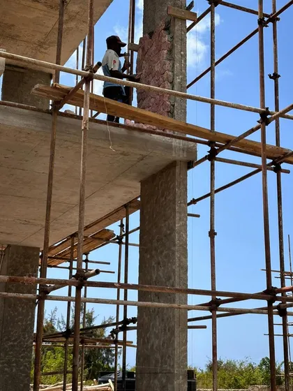 A worker on scaffolding applies stone to a column. This high-level work requires skill and a good head for heights, all part of the process of realizing the design on site.