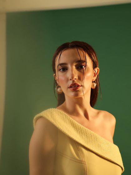 A close-up beauty shot with a wet-hair look and minimalist makeup. This highlights the model's features and the simple elegance of the off-shoulder yellow top.