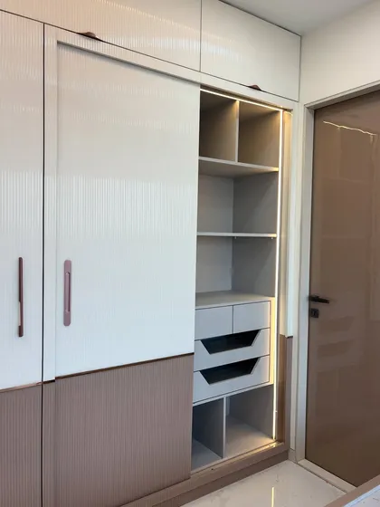 A combination wardrobe with both sliding and hinged doors. This image shows the interior of the sliding section, complete with drawers and shelves, illuminated by an internal sensor light.