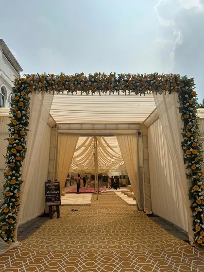 A grand entrance sets the tone for the entire event. We designed this welcoming floral archway for a large religious gathering, using a mix of yellow and white flowers to create an elegant and inviting passage for guests into the beautifully draped tent.