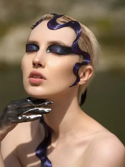 A close-up portrait from the 'Siren' shoot, detailing the glittery purple eyeshadow, single rhinestone, and the dark, textured hand makeup.
