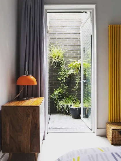 This design shows how even the smallest light well or side yard can become a green feature. Viewed from the bedroom, this narrow space is transformed with a brick wall and climbing plants, bringing nature right to the window.