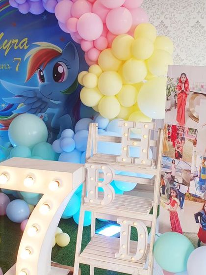 A whimsical My Little Pony-themed seventh birthday. The decor features a Rainbow Dash backdrop, a rainbow balloon arch, and a large light-up number '7'.