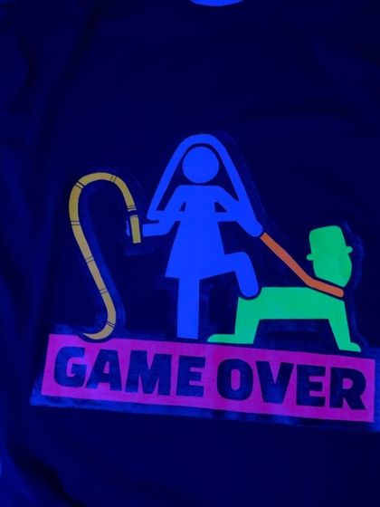 A close-up of the "Game Over" T-shirt under blacklight, showing how the neon paints glow for a party-ready effect.