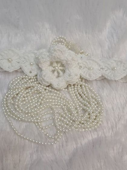 I designed this piece to be extra special. It's a white floral crochet headband with elegant pearl tassels that drape beautifully, perfect for a photoshoot or blessing ceremony.